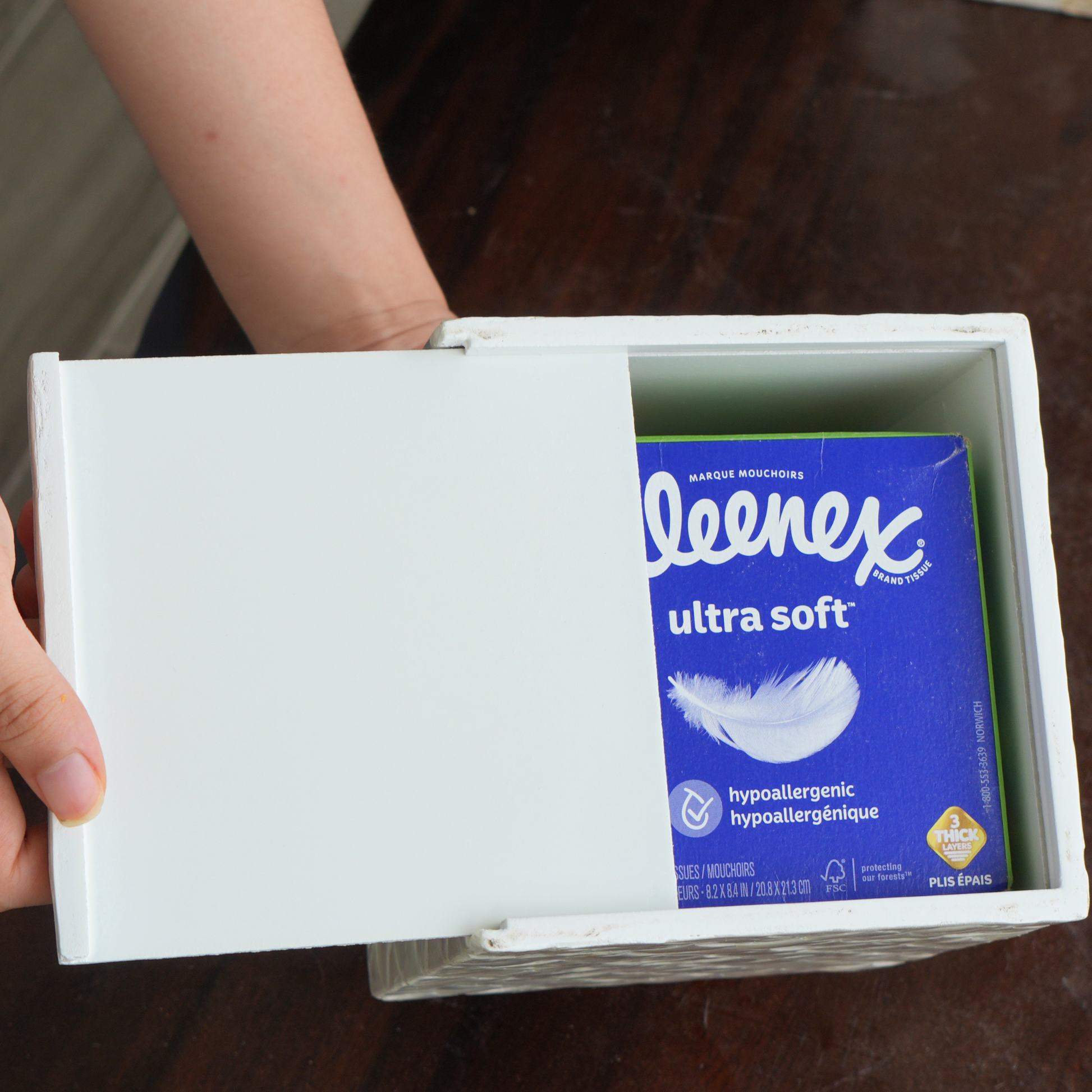 A hand slides open a white capiz shells tissue cover box, revealing a 60-count tissue box of Kleenex Ultra Soft tissues inside.