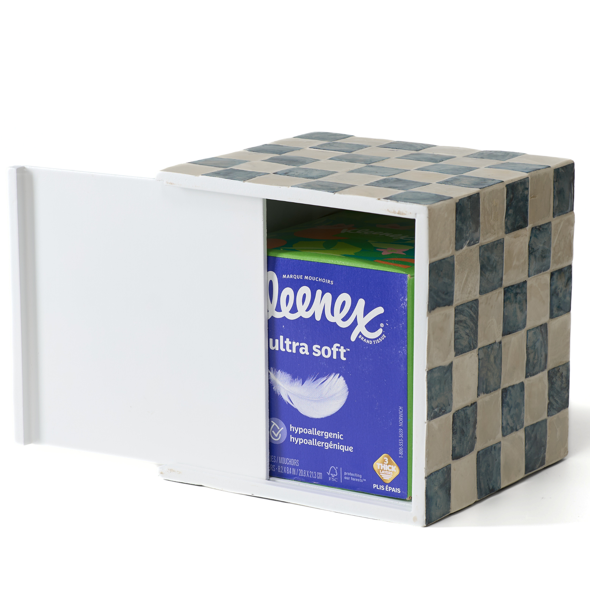 A white capiz shells tissue dispenser with a checkered navy blue and beige patterned exterior, shown with its slider open and a box of Kleenex 60-count Ultra Soft tissues inside.